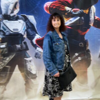 Photo of Karen Vasquez at an art gallery, in the background is a giant photo of Destiny characters.